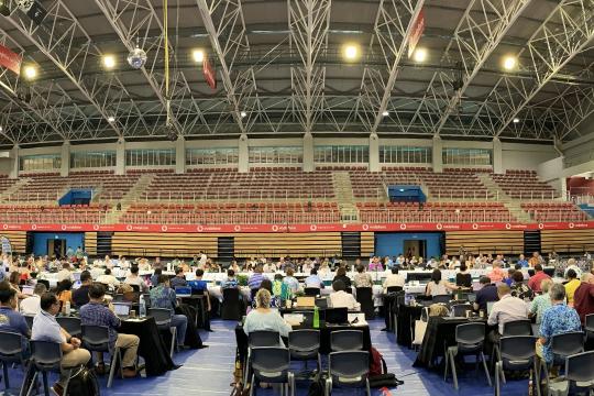 Delegates from various nations throughout the Pacific Ocean are seated in a large arena with placards identifying which nation or group they represent at the 21st Western and Central Pacific Fisheries Commission (WCPFC) meeting.