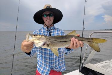 a man in a hat holding a large snook