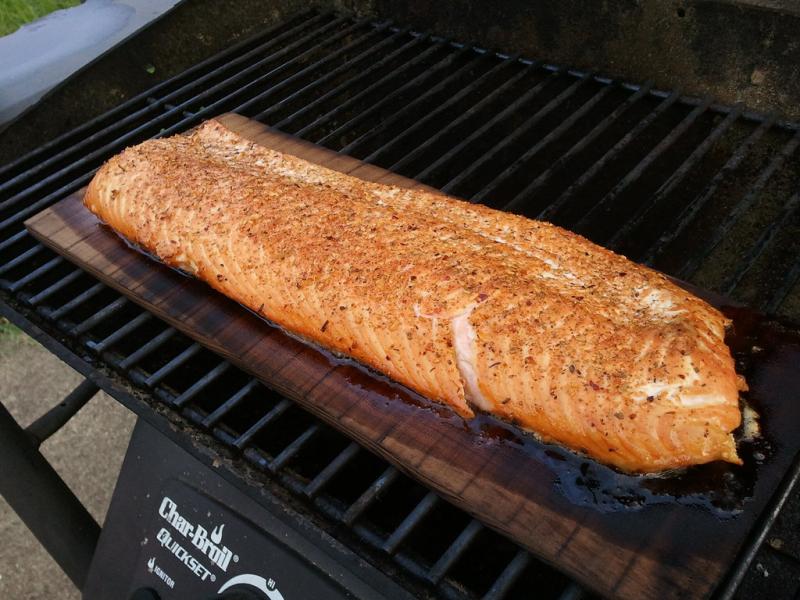 Photo of a salmon fillet on a plank and outdoor grill. 