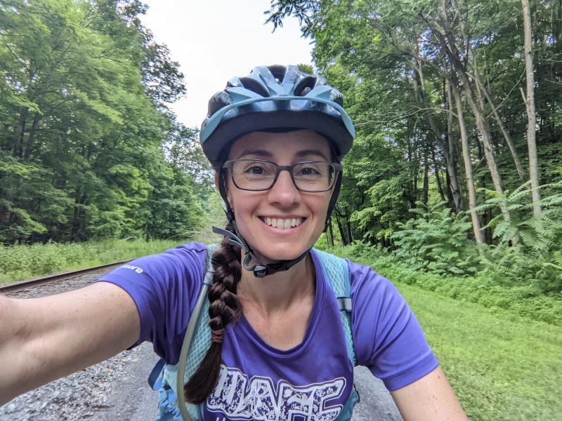 Selfie of woman wearing bike helmet riding her bike with trees and grass in the background